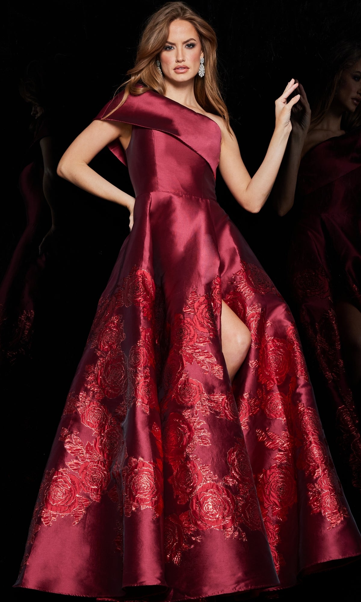 A woman poses against a black background in the Jovani Long Red One-Shoulder Prom Ball Gown 09610, a floor-length gown featuring floral embroidery and a thigh-high slit.